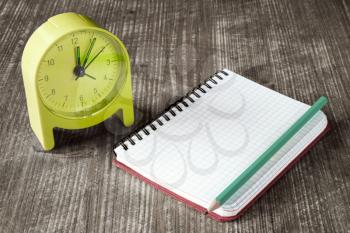 Time management concept: green alarm clock, pencil and notebook