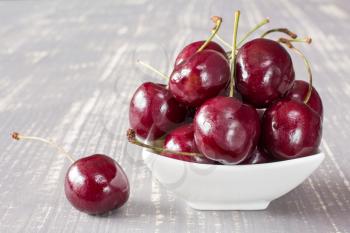Cherries in white bowl on the grey wooden surface