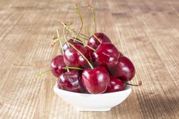 Cherries in white bowl on the wooden background