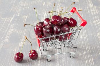 Shopping cart with cherries on the grey wooden background