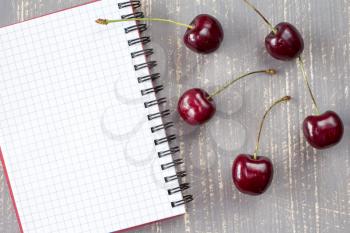  Fresh cherries and blank notebook for recording on the grey wooden background