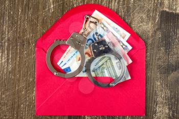 Red Envelope with Euro bills and handcuffs over wooden background