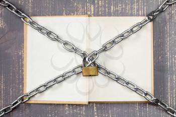   Open book with chain and padlock on wooden background.