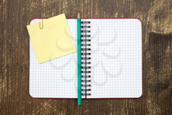 Open notebook with sticky note and pencil on wooden background