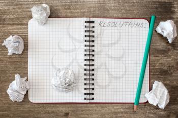  Notebook for RESOLUTIONS and crumpled paper on the wooden desk