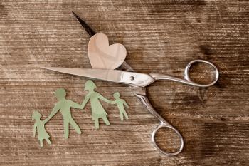 Scissors,cutout paper family and heart on wooden background