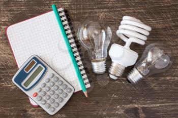 Three different light bulbs and notebook with digital calculator