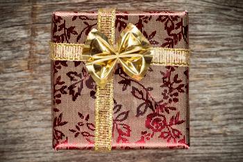 Gift box with golden bow. On old wooden background.