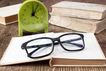 Books with glasses and alarm clock on the desk