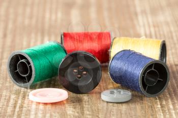 Spools of colored thread and buttons on wooden background. 