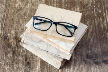 Top view of books and reading glasses on the wooden background.