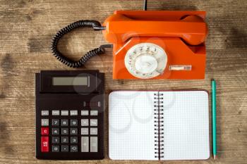 Rotary telephone, calculator and blank notebook on wooden table. Top view.