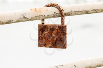 Old rusty padlock hanging on metal bar 