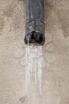 The old drain pipe with frozen water against the wall