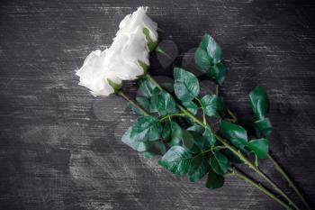 Three artificial white roses on wooden background