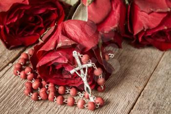 Catholic rosary and old roses on wooden background 