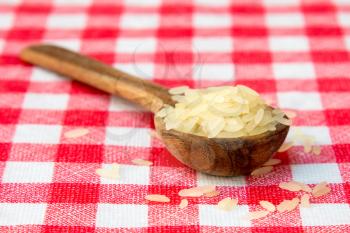 Raw parboiled rice in a wooden spoon on checkered tablecloth