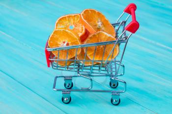 Dry orange with shopping cart on blue wooden kitchen table background