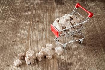 Shopping cart with brown cane sugar  on wooden background