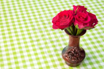 Bouquet of red roses in a vase on checkered tablecloth background