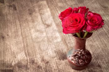 Bouquet of red roses in a vase on wooden background