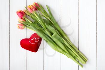 Spring tulips and plush heart on white wooden background