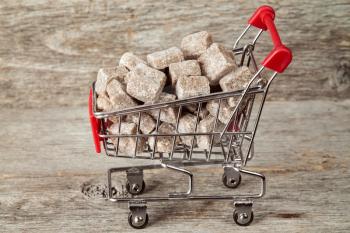 Shopping cart full of brown cane sugar on wooden background