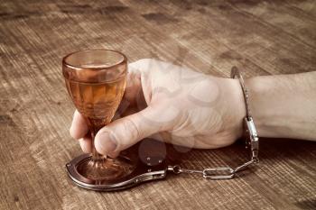 Alcohol addiction, hand handcuffed with an alcohol glass