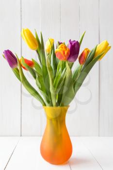 Bouquet of colorful tulips in vase on white wooden background