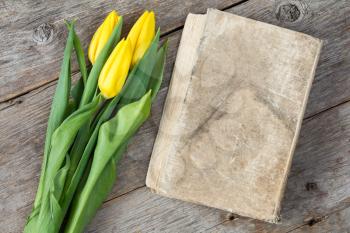 Bouquet of tulips with old book on grey wooden table