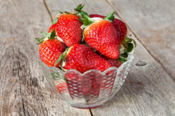 Fresh juicy strawberries in glass bowl on wooden background