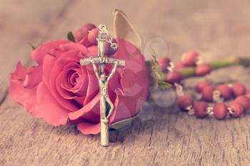 Silver crucifix and single rose on wooden background.Pastel colors.