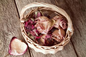 Buds of faded roses in wicker basket on wooden background