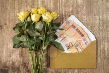 Bunch of roses and envelope with money over wooden background