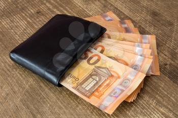 Money in black leather wallet on wooden background 