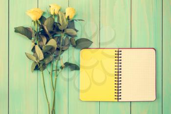 Blank notebook and three roses on the blue wooden background