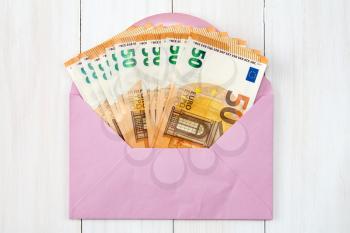 Pink envelope with Euro bills over wooden background