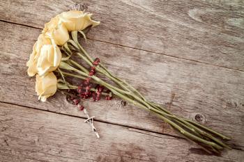 Silver crucifix and yellow roses on old wooden background