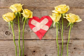 Human feeling repairing concept - red broken heart with yellow roses on wooden background