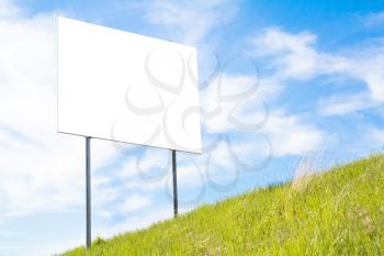 Big blank sign board on a background of green grass and blue sky