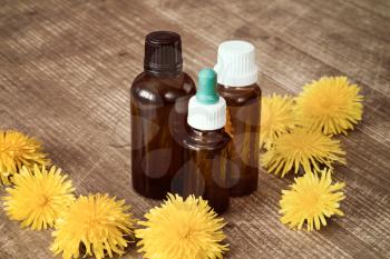Dandelion extract in a small bottles with yellow flowers on wooden background