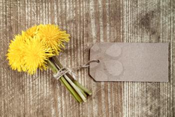 Dandelion flowers with paper tag on wooden table