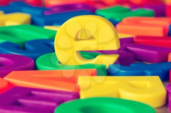 Yellow letter e in a pile of other colorful plastic letters.