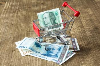  Norwegian currency and shopping cart on wooden background