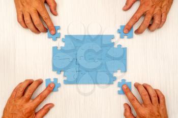 Four hands collects jigsaw puzzle. Concept for teamwork or building a success.