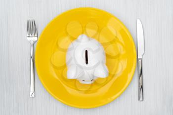 Savings consumer concept. Piggy bank on the dinner plate with fork and knife.
