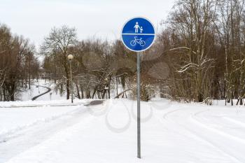 A sign of a bike path and a pedestrian in the park in winter