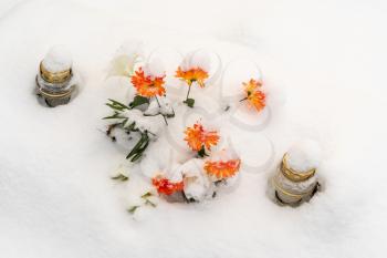 Winter grave in cemetery with snow covered flowers and candles