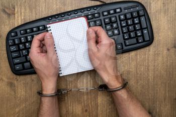 Hacker concept, punishment for cybercrime with hands in handcuffs above computer keyboard