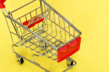 Close-up view of empty shopping cart on yellow background